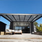 Modern outdoor patio with pergola and seating area under a clear blue sky.